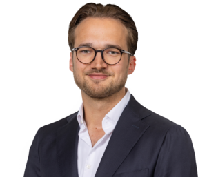 Porträt eines lächelnden Mannes mit Brille und Sakko vor weißem Hintergrund.