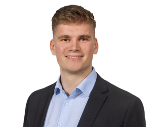 Ein lächelnder Mann im Anzug und blauem Hemd vor weißem Hintergrund, Portraitfoto.