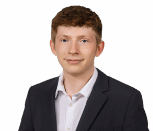 Junger Mann im Anzug vor weißem Hintergrund, lächelnd und mit kurzem, lockigem Haar.