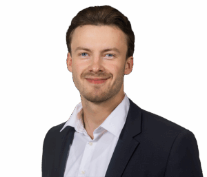 Mann in Anzug lächelt in die Kamera, vor weißem Hintergrund, Portraitaufnahme.