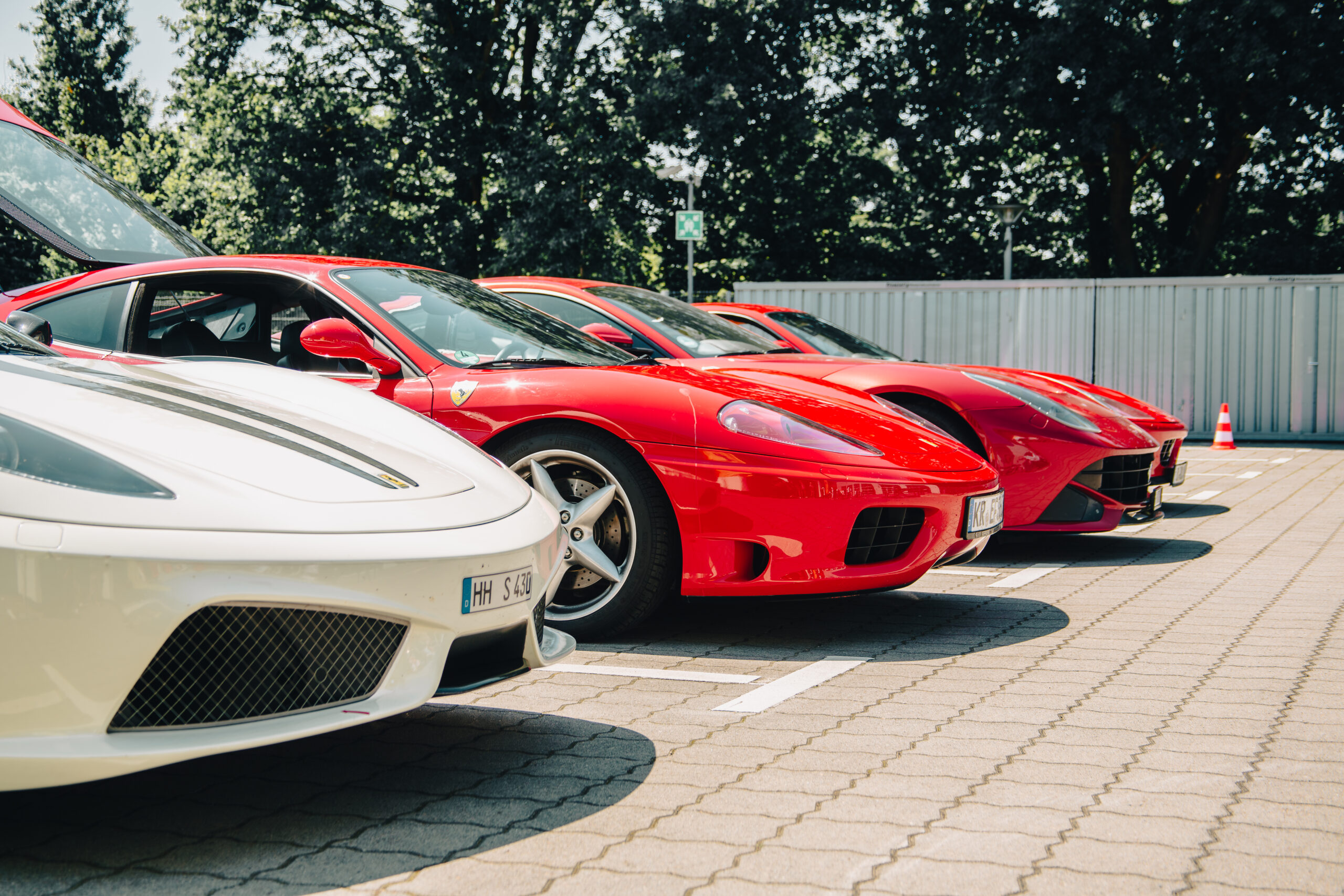 Rote und weiße Ferrari-Sportwagen nebeneinander auf einem Parkplatz bei sonnigem Wetter.