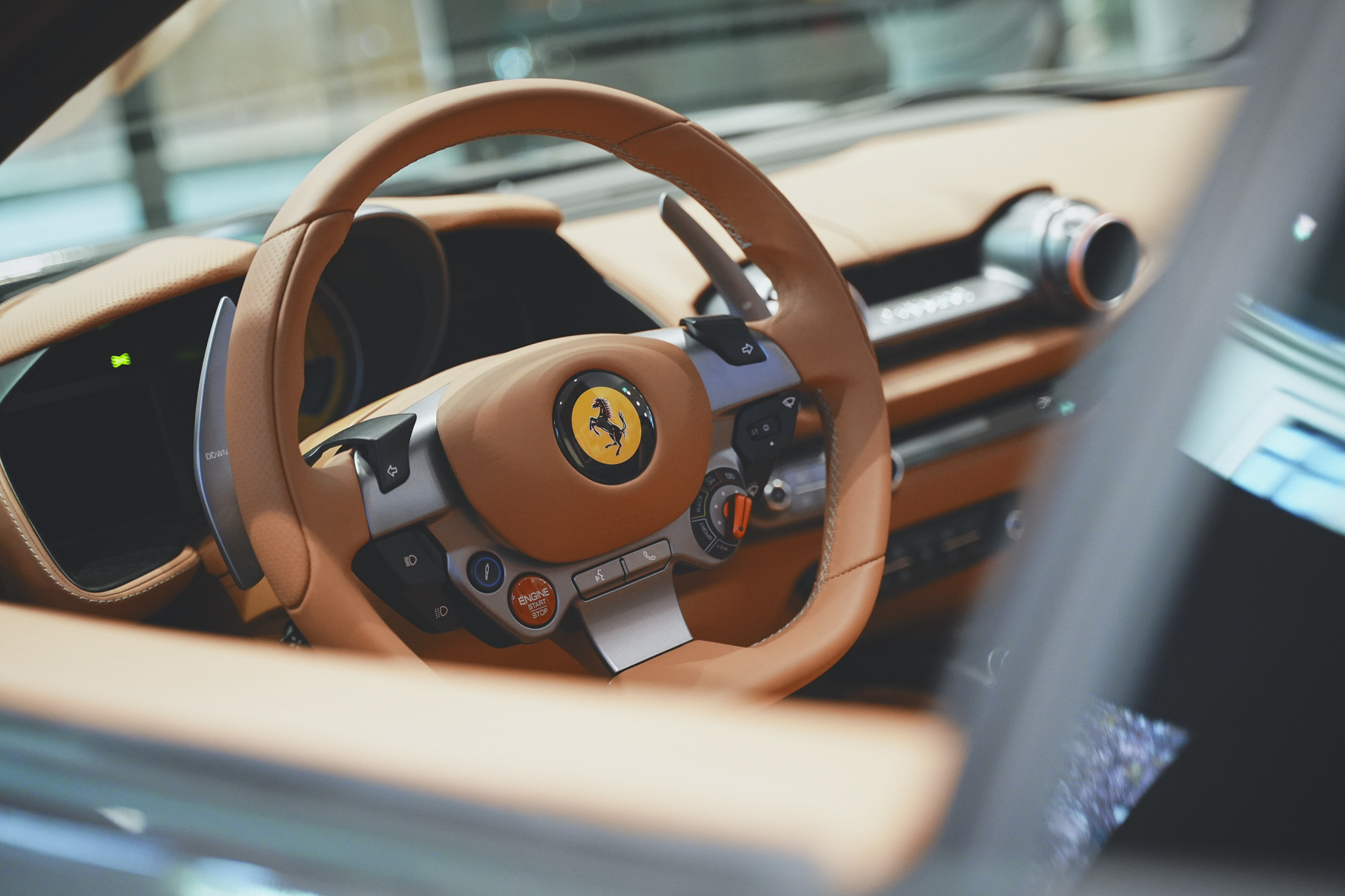 Lenkrad und Innenraum eines Ferrari-Sportwagens mit braunem Lederdesign und Mittelkonsole.