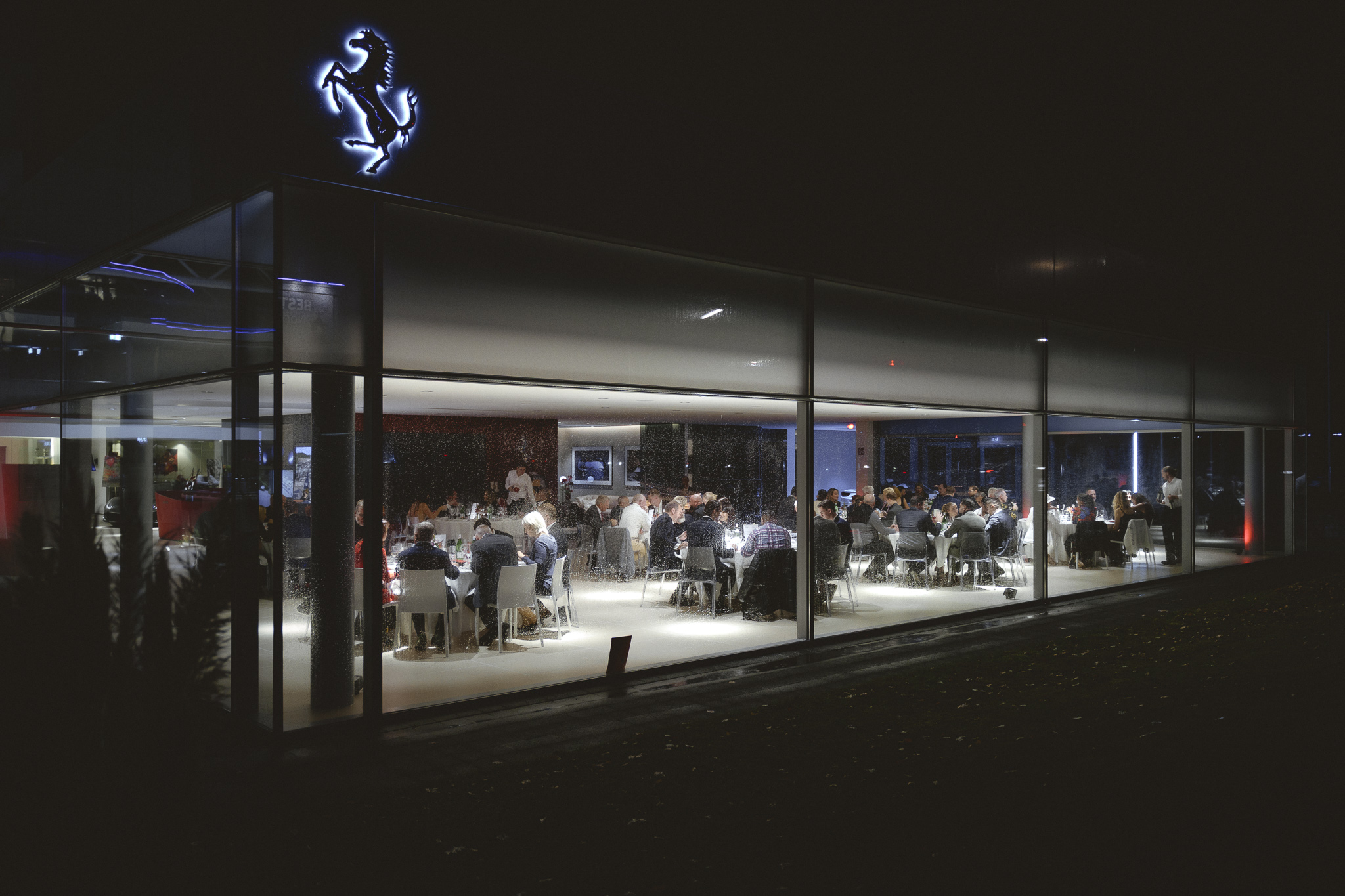 Menschen bei einer Veranstaltung in einem Ferrari-Gebäude mit gläsernen Wänden bei Nacht.