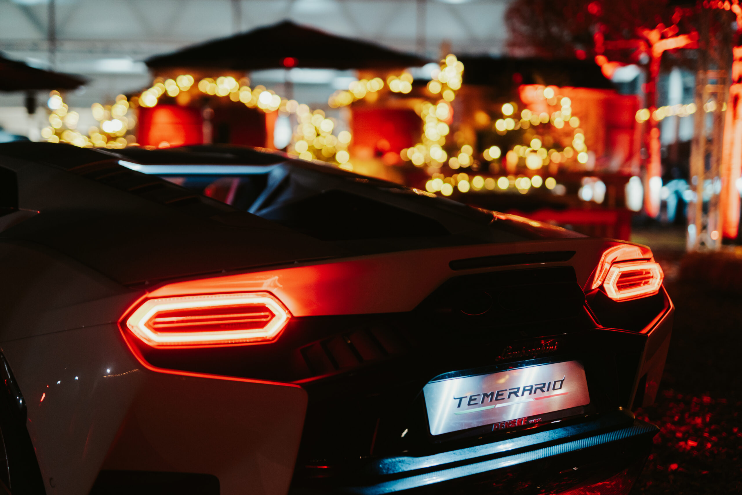 Sportwagen mit leuchtenden Rücklichtern in einer nächtlichen, festlich dekorierten Umgebung.