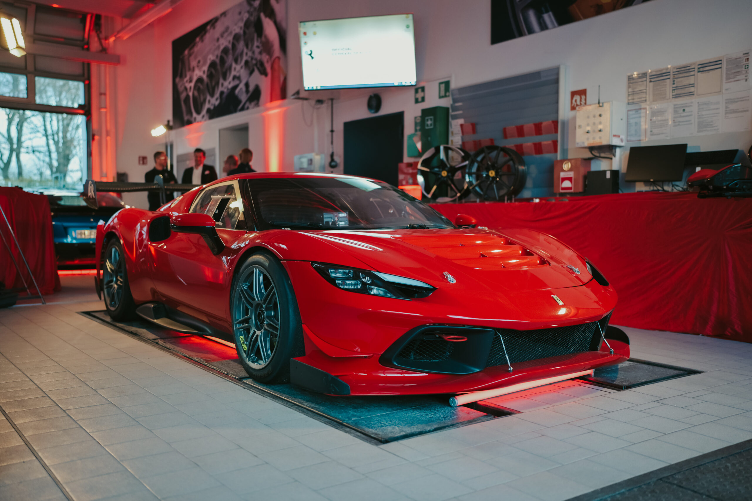 Roter Ferrari-Sportwagen im Showroom, flankiert von roten Wänden und Dekorationen, mit elegantem Design und sportlicher Optik.