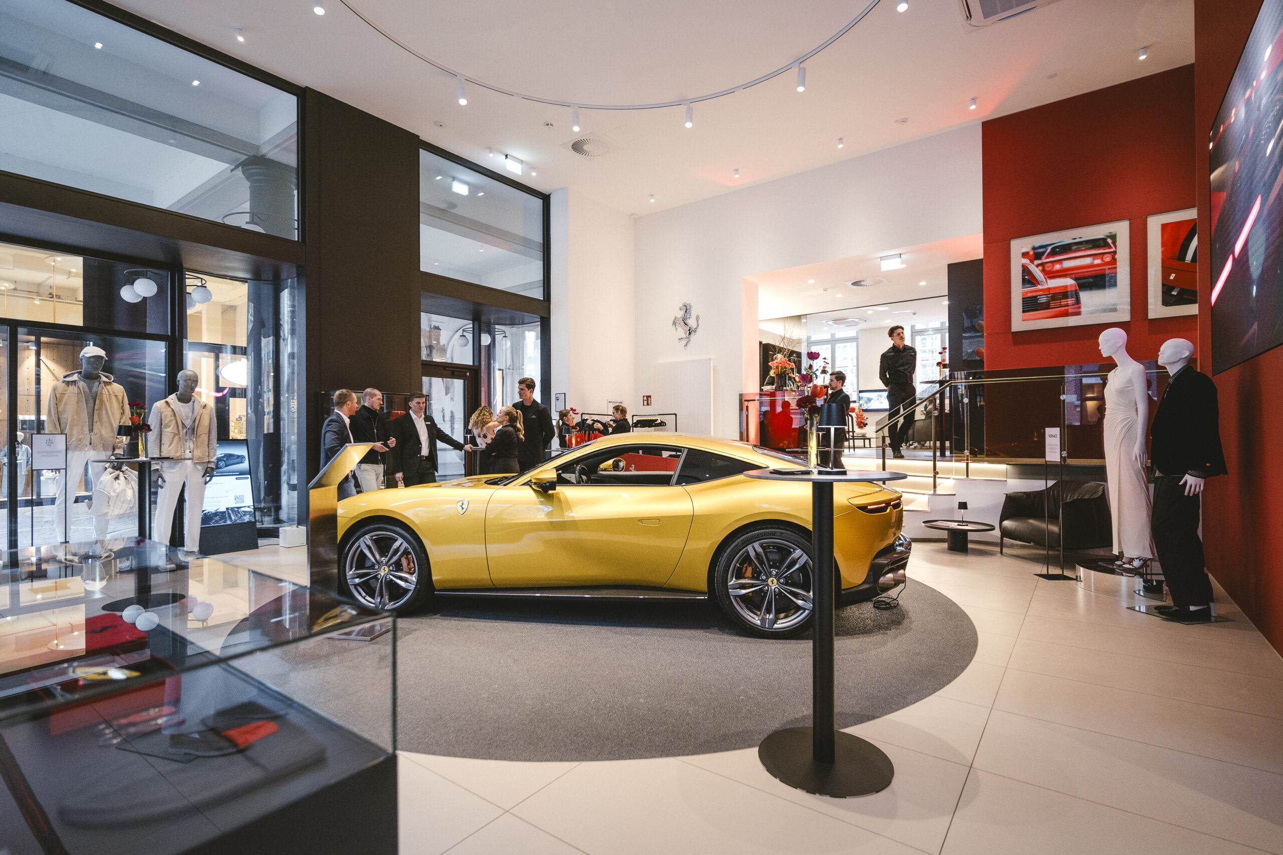 Gelber Ferrari in einem modernen Showroom mit Menschen, die das Auto begutachten, umgeben von eleganter Einrichtung.