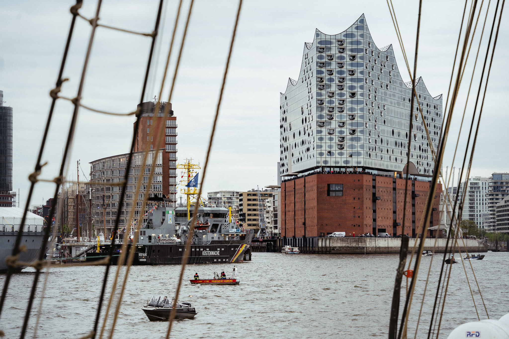 Elbphilharmonie Hamburg, aufgenommen von einem Segelschiff aus mit Hafen im Vordergrund und Wolkenhimmel.